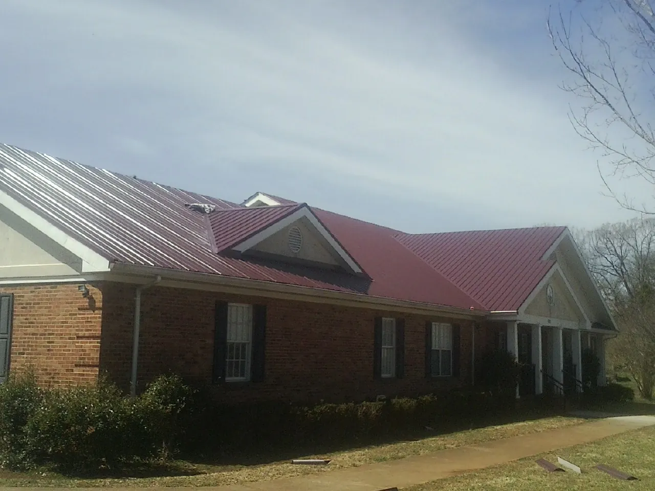 Red metal roof with gabled entries on a long brick building, from a Hail Damage Roof Repair job in Fayette