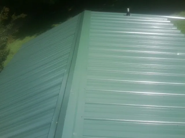 New green metal panels meeting at the ridge of a roof — Flat Roof Repair work by our crew in Fayette
