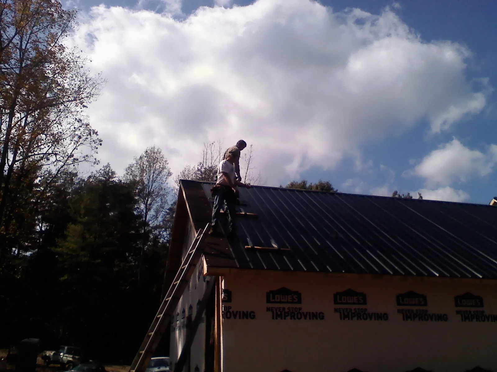 Roofer fastening dark metal panels high against a cloudy sky, from a Roof Inspection job in Fayette
